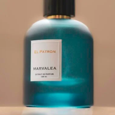 A chic teal perfume bottle labeled El Patron Marvalea, resting elegantly on a reflective surface.
